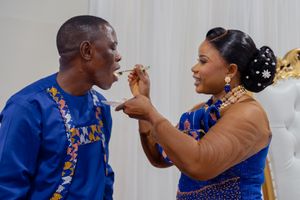A couple in matching blue attire feed each other cake during their wedding reception celebration.
