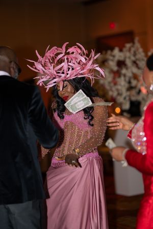 Person in a sparkly pink formal gown with feather fascinator dancing at an elegant evening event.
