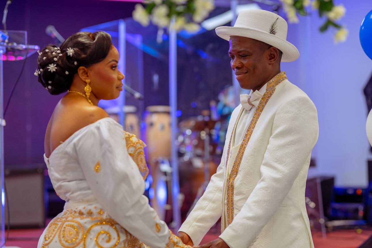 Couples in formal attire dance together at an elegant event with purple lighting and decorative elements.