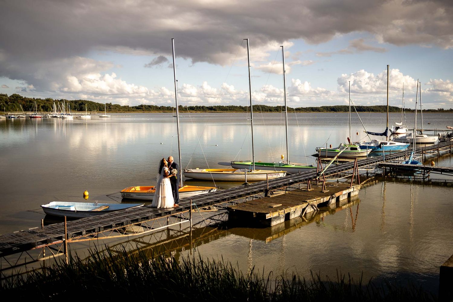 Dramatic panorama of boats docked at a marina under stormy clouds at sunset.