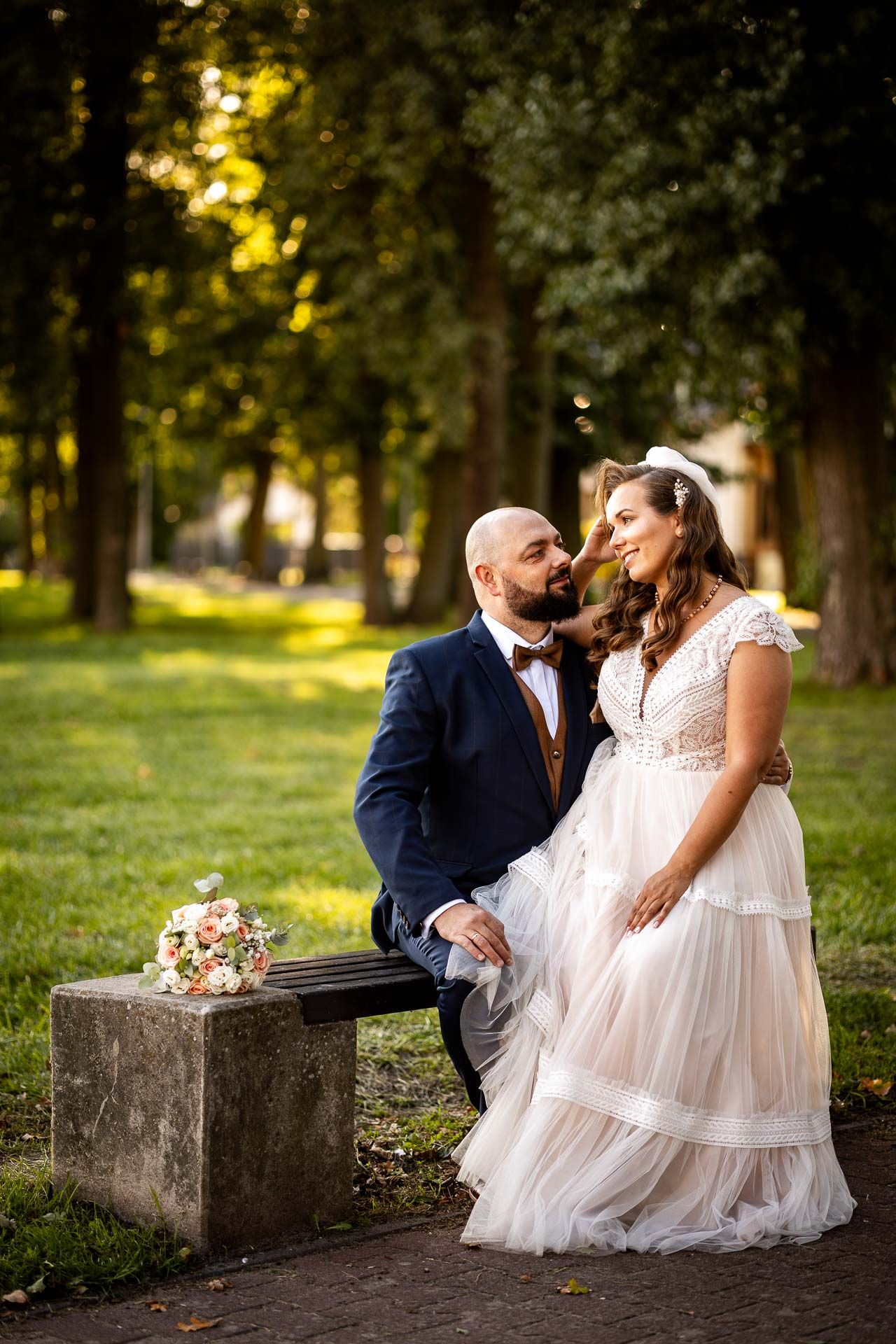 Romantic wedding couple sitting on stone steps in a sunlit garden setting.
