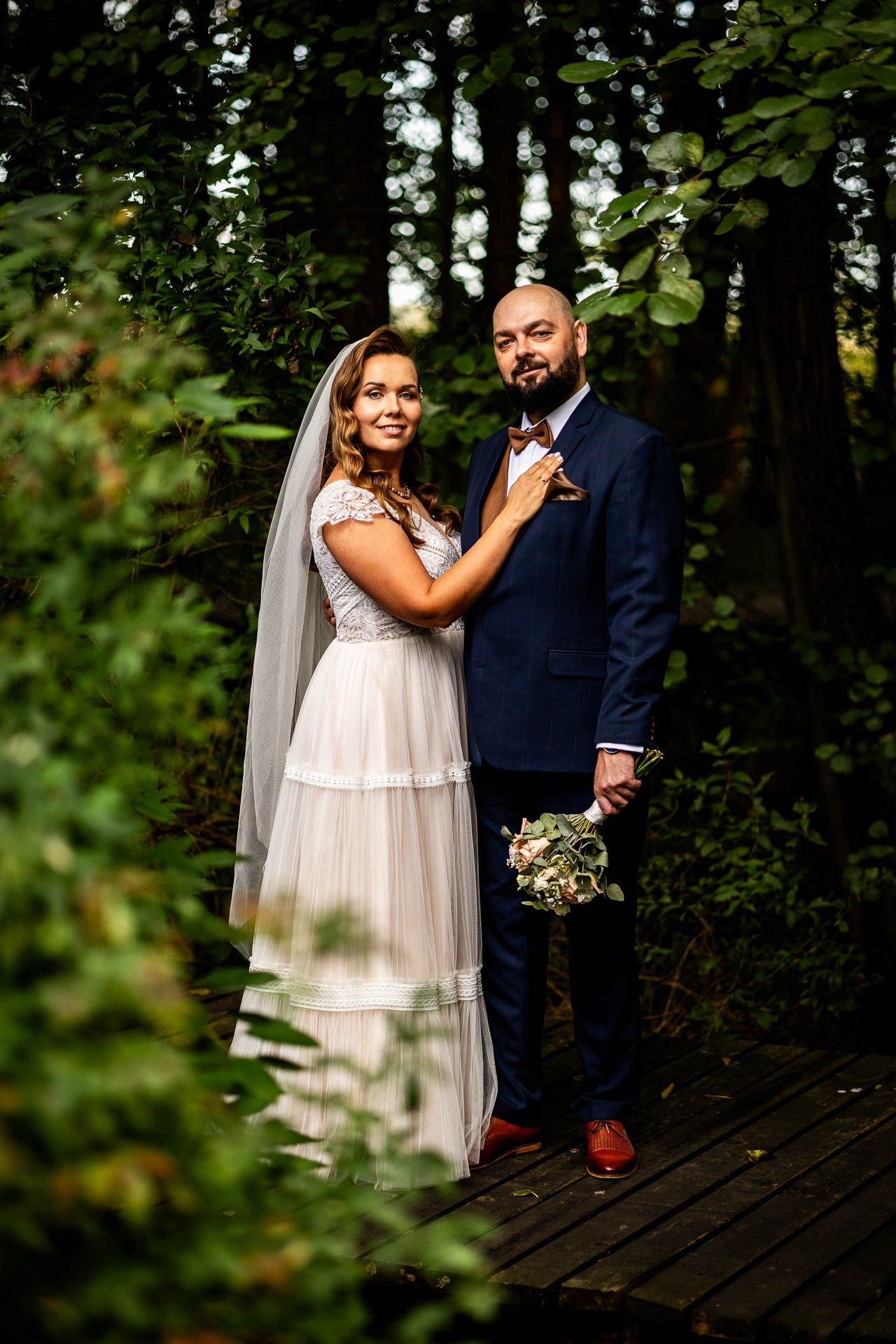 Wedding couple sharing intimate moments on a wooden boardwalk surrounded by lush greenery.