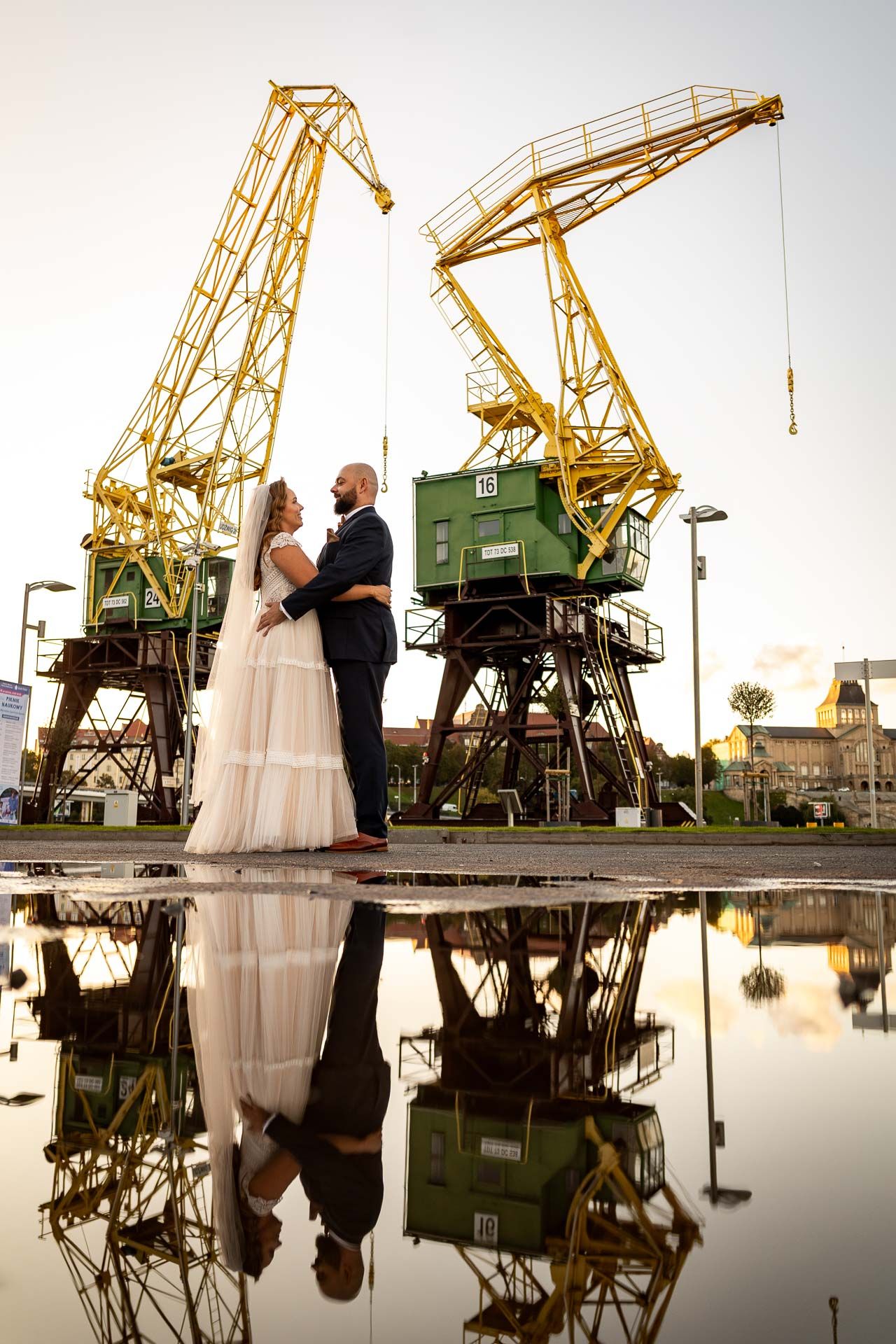 Wedding portraits with industrial crane reflections in water creating dramatic symmetrical compositions.