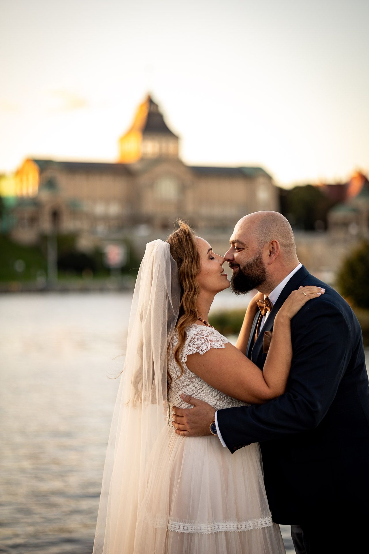 Romantic sunset wedding portraits by the waterfront with historic buildings in background.