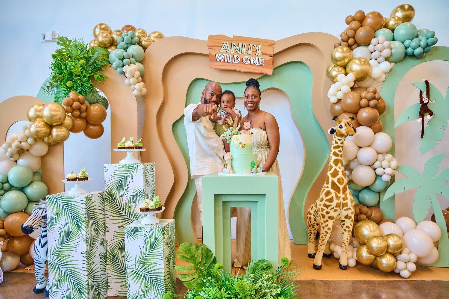Safari-themed party decoration with balloon arches and palm leaves in soft beige and green tones.