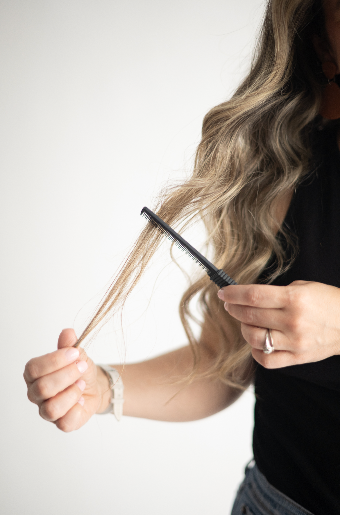 Hands holding and combing through long wavy blonde ombre hair against a white background.