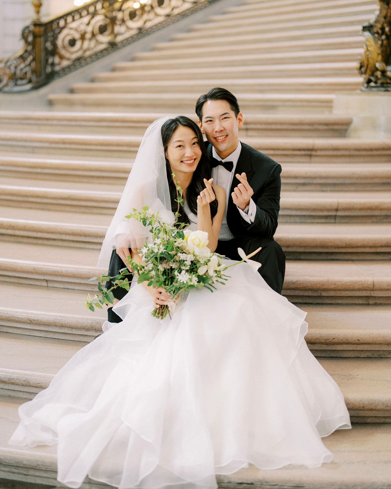 A bride and groom pose joyfully on ornate marble steps during their wedding photoshoot.
