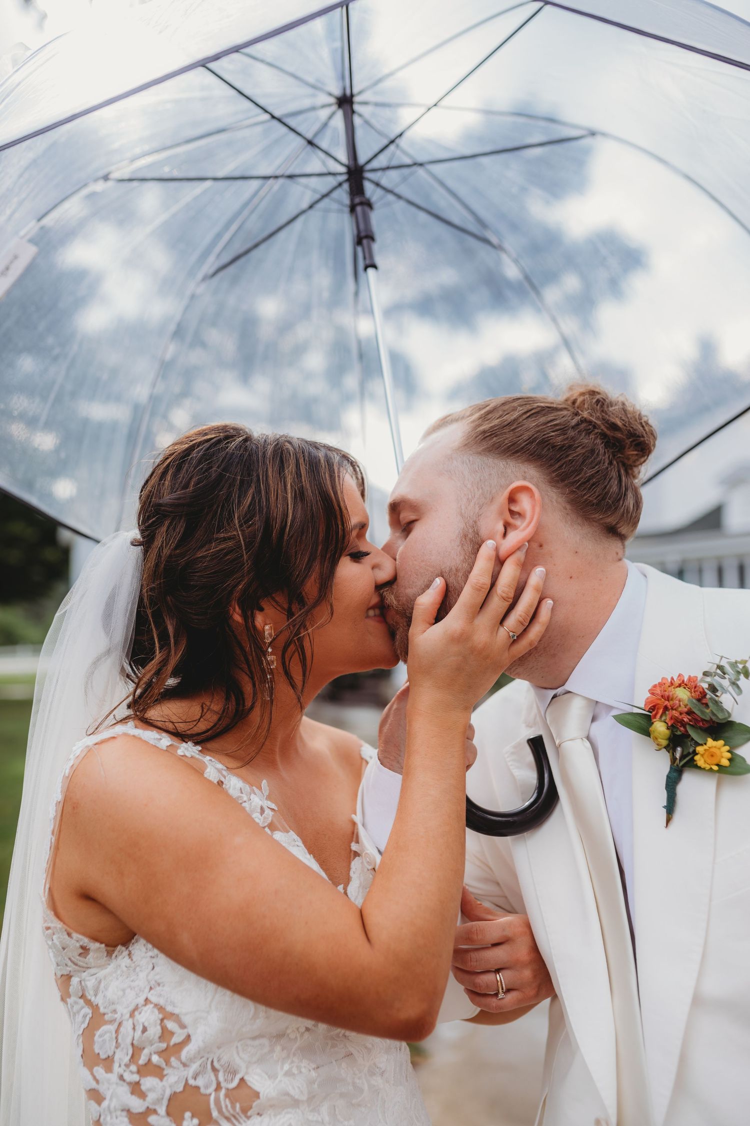A romantic kiss under a clear umbrella on a cloudy wedding day.