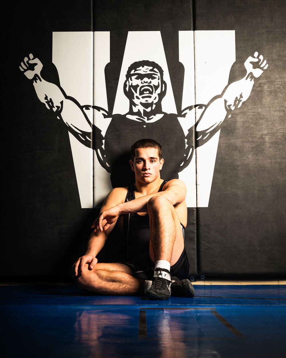 Athletic figure performs strength training exercises on floor against dark wall with dramatic lighting and shadows.