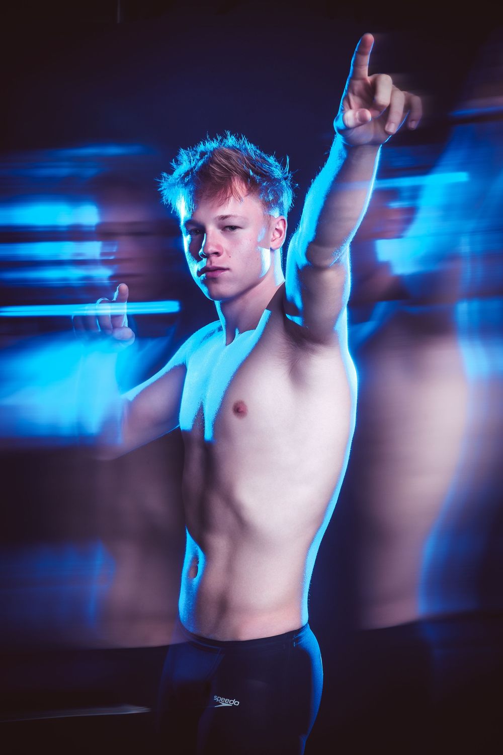 Artistic portrait in blue lighting shows shirtless dancer in motion against dark background with motion blur effects.
