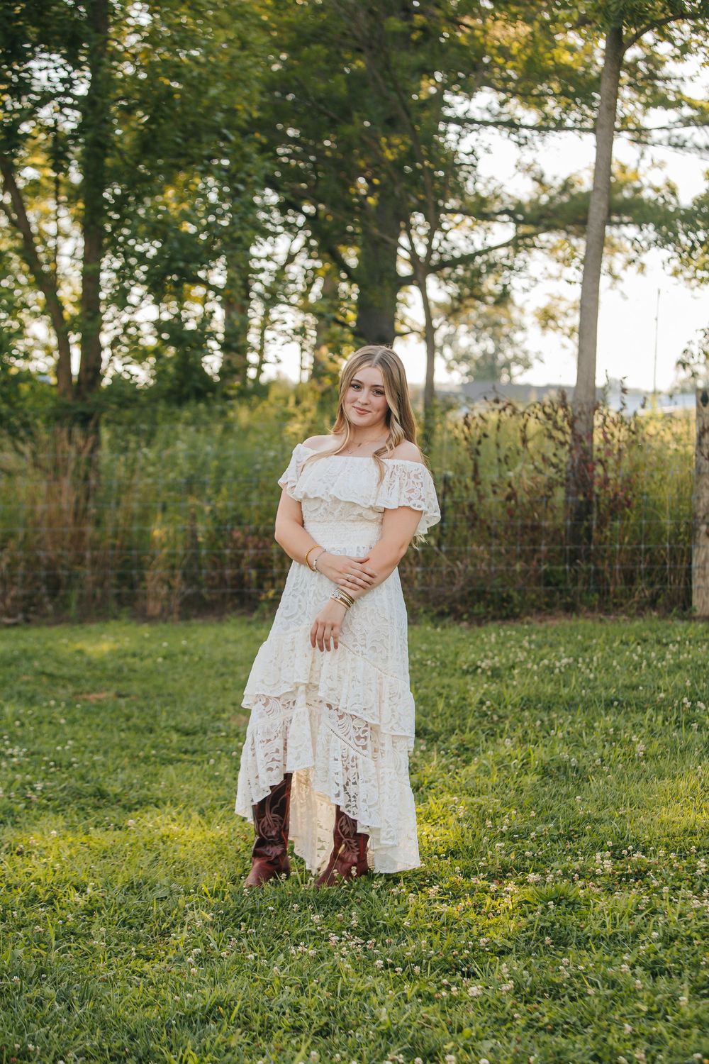 A white lace dress stands out against a lush green field with trees in the background during golden hour.