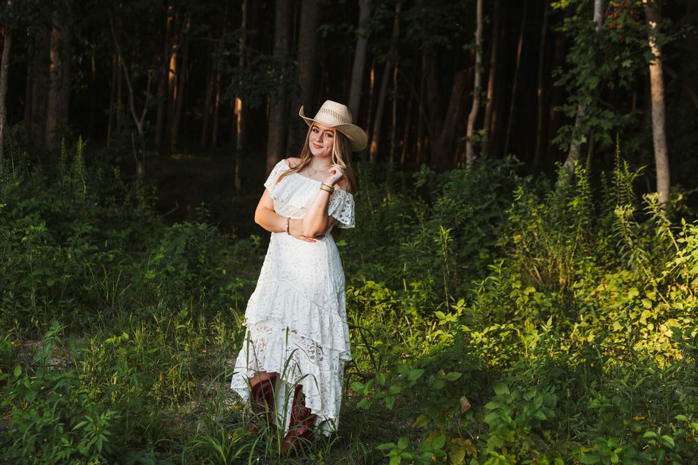 A dreamy summer scene in a forest with a white lace dress and sunhat against lush greenery and golden sunlight.