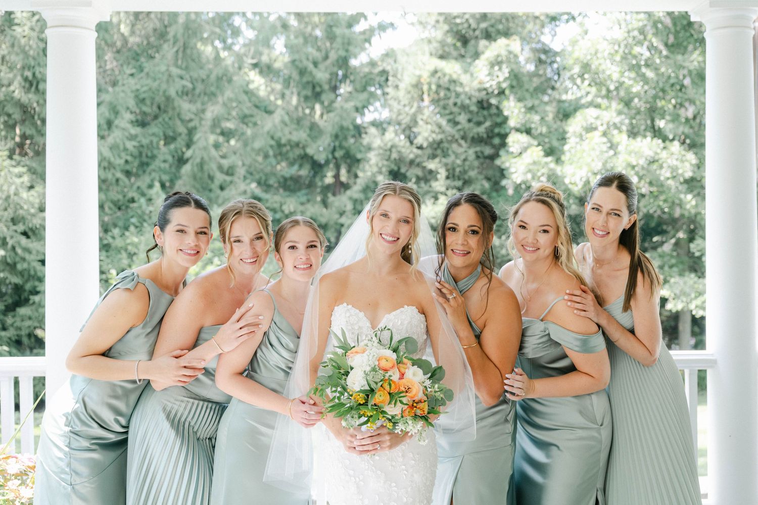 Wedding party in sage green dresses poses together in a series of candid moments on a porch. - Lake Forest