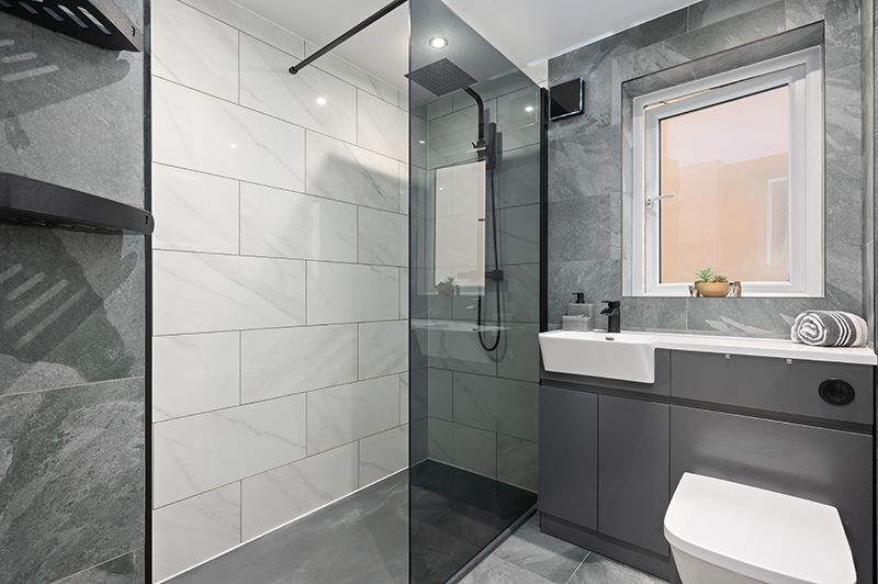 Modern bathroom interior with gray marble-look tiles, glass shower enclosure, and sleek fixtures in minimalist design.