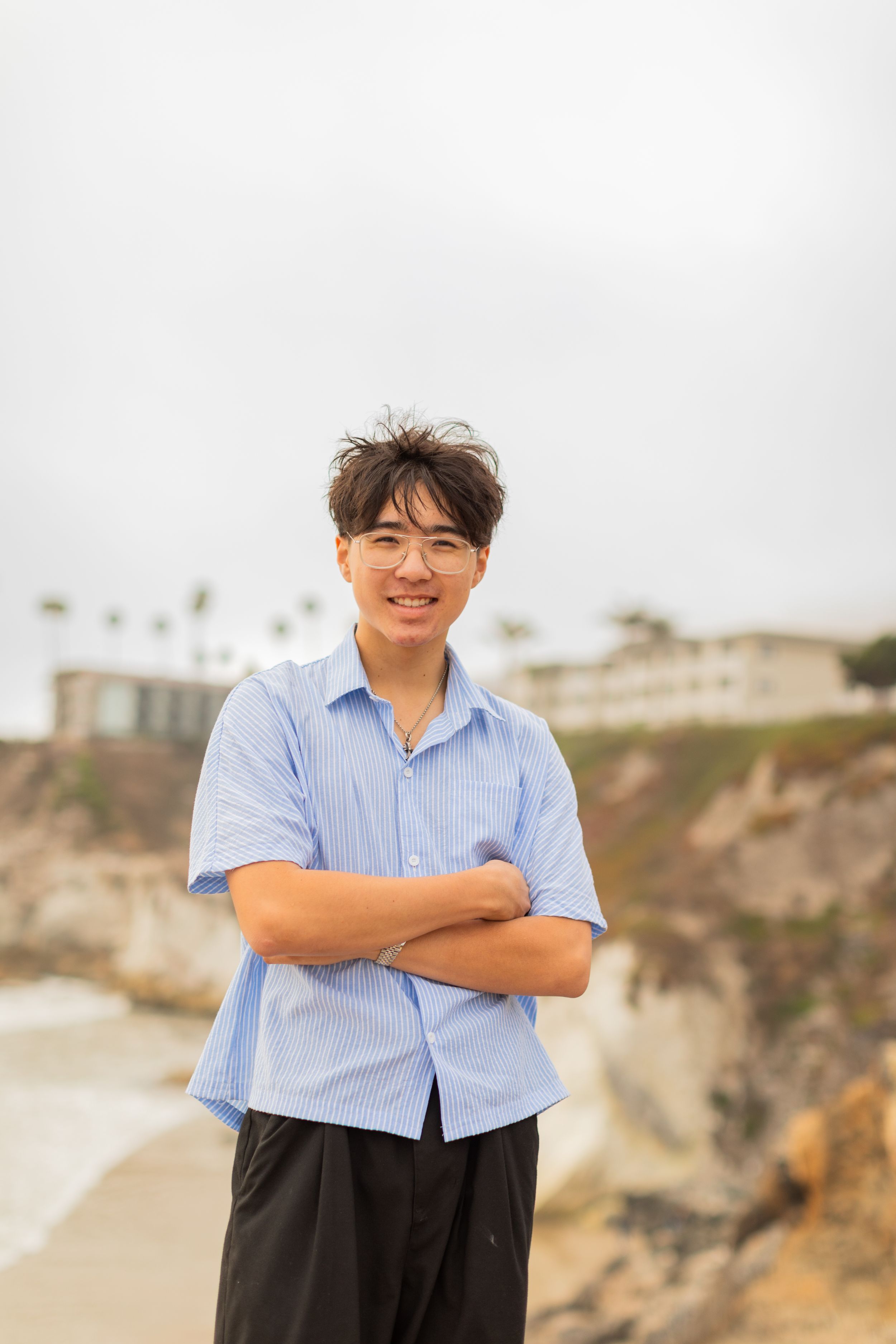 Person in light blue shirt smiling on coastal cliffs with ocean view background.