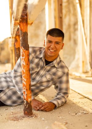 A person in plaid shirt poses near wooden pillars during golden hour.