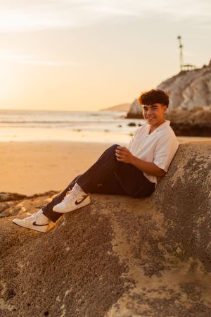 Person relaxing on coastal rock formation during golden sunset.