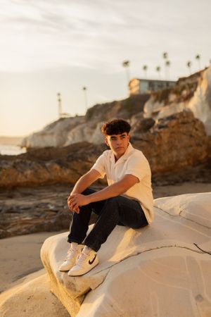 Person in casual attire sitting on rocky beach formation at sunset.