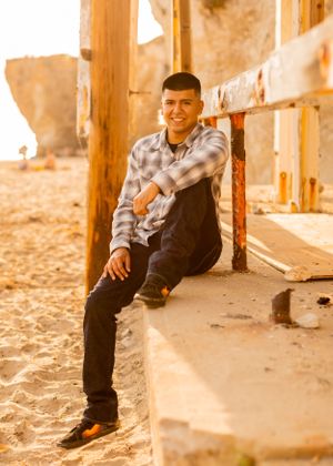 A person in casual attire sits on wooden beach structure during sunset.