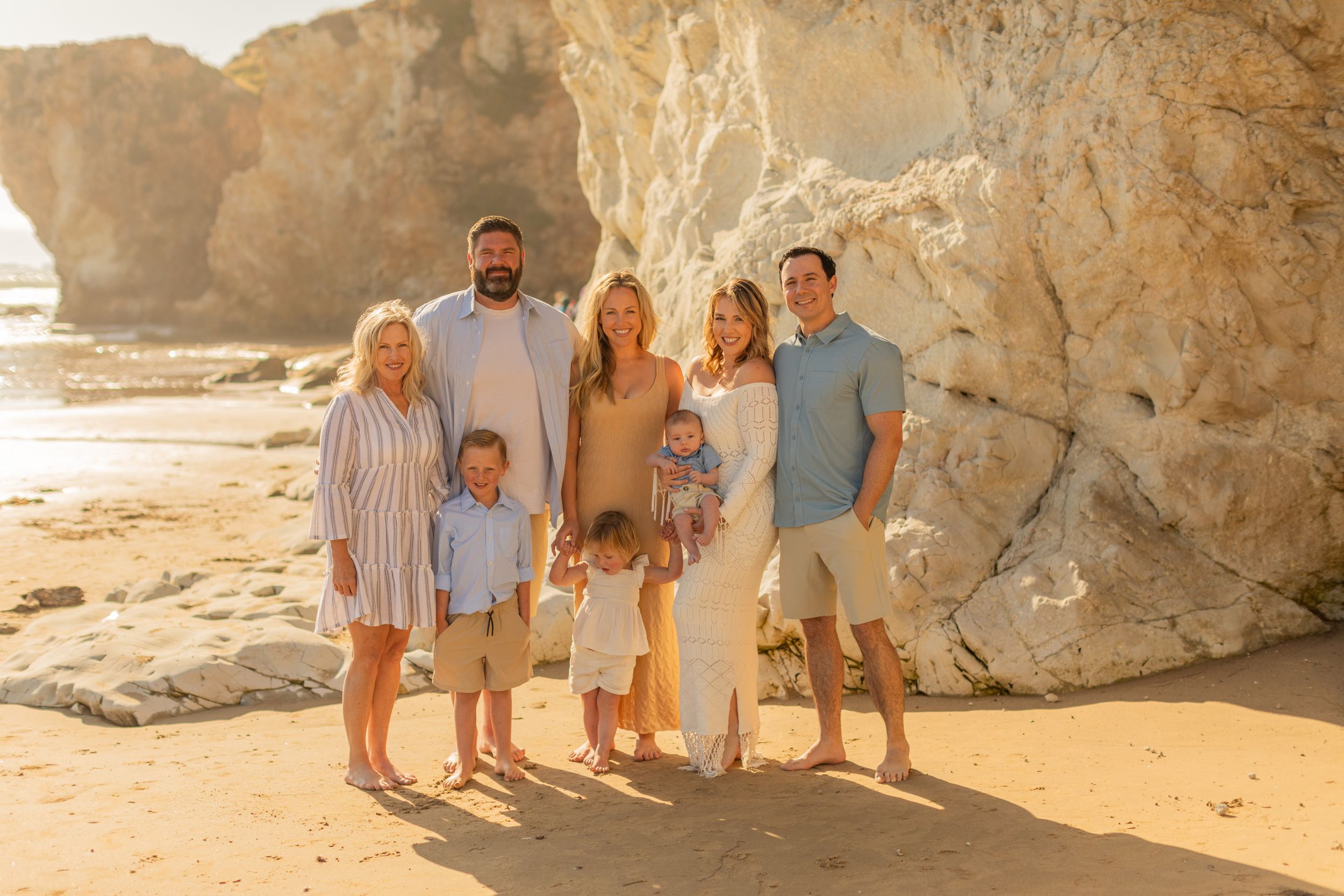 A group poses together on a beach with dramatic coastal rock formations in the background.