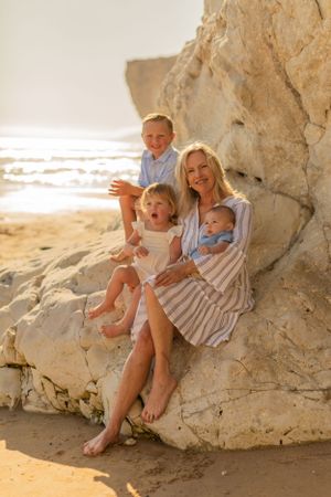 Family group sits together on beach rocks during golden hour photography session.