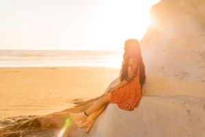 Woman in orange dress sits on coastal stone steps during golden hour.