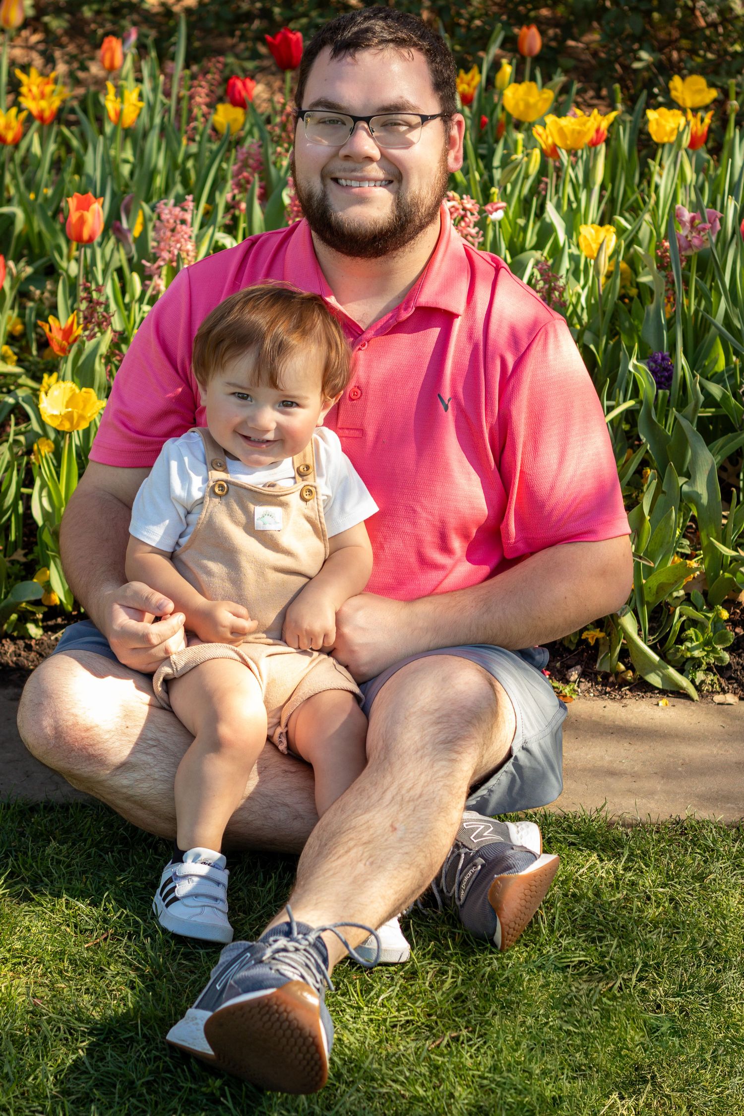 Family enjoying springtime together on grass near colorful blooming tulip garden on sunny day.