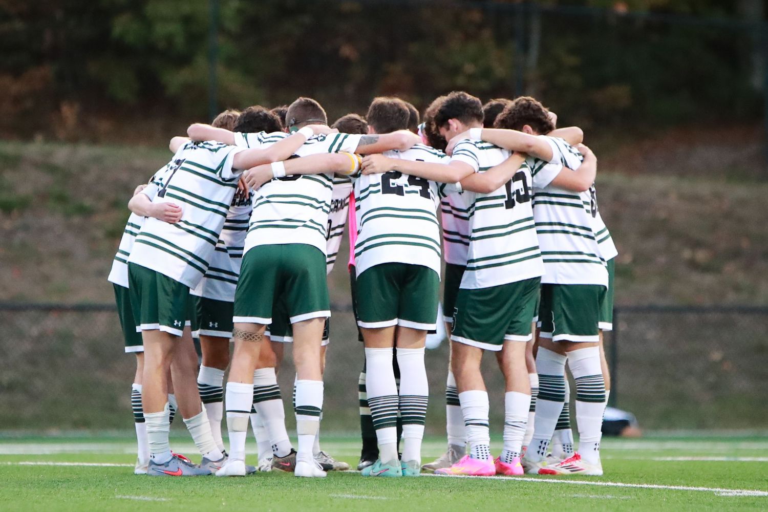 Soccer team huddles together in a circle before the game on a grass field.