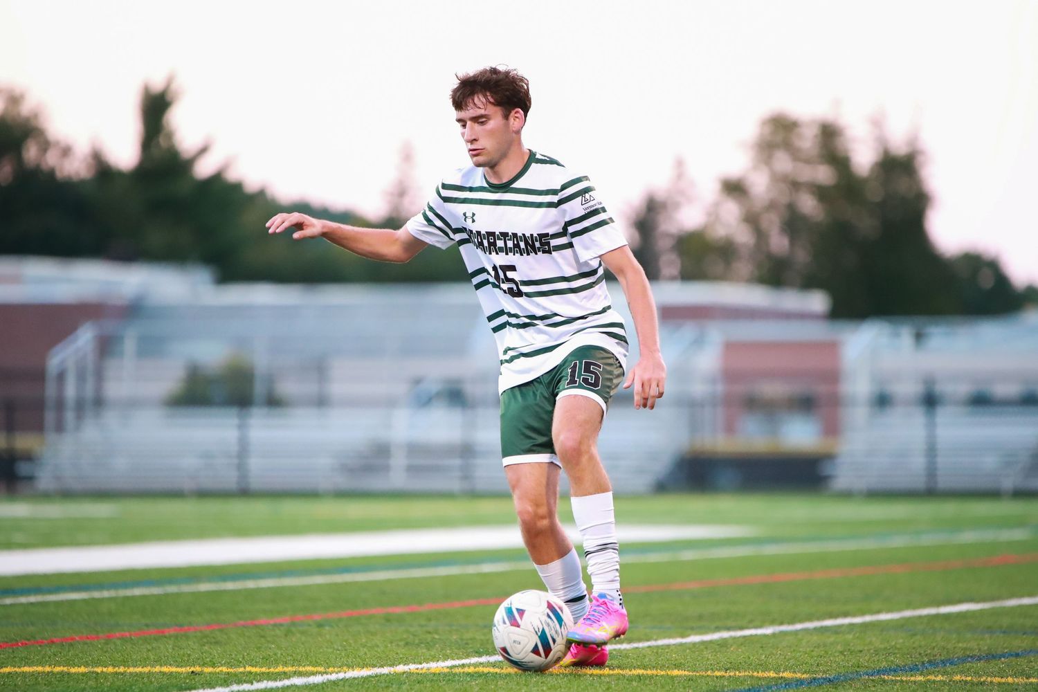 Soccer player prepares to kick the ball during a match at sunset on an outdoor field.