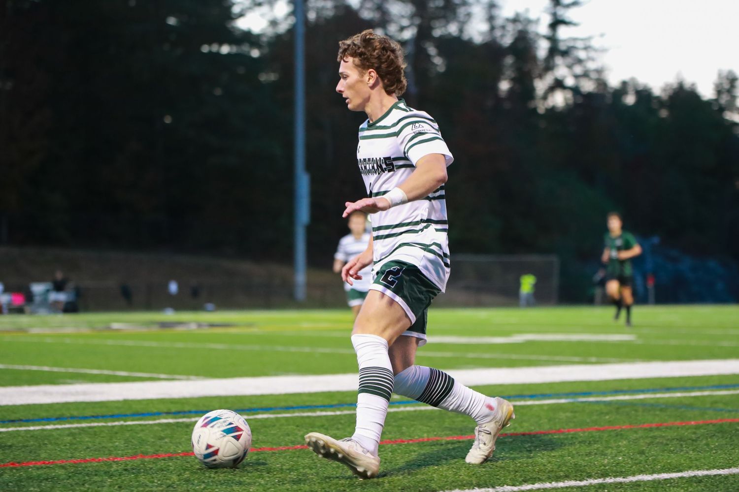 Soccer player in white striped uniform takes a shot on goal during a competitive match.