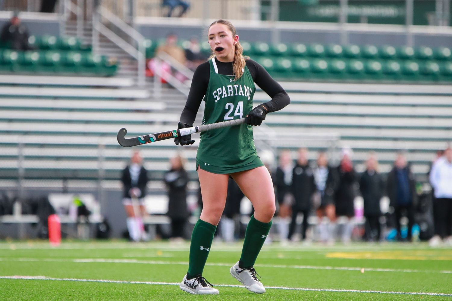 Field hockey players in green and white uniforms compete during a match on artificial turf.