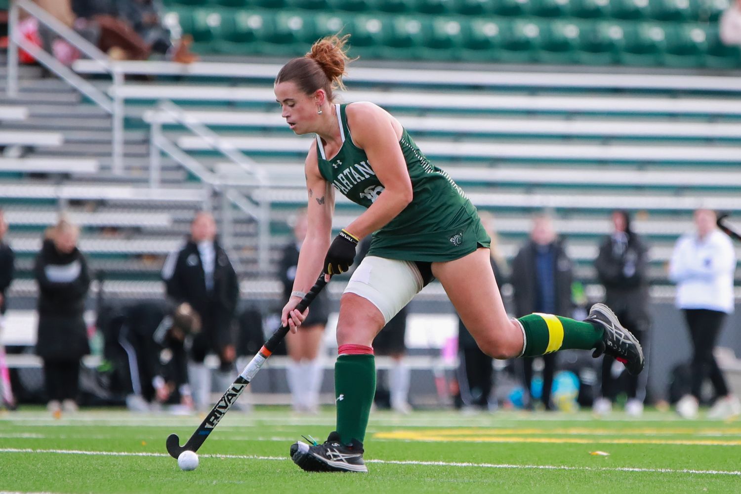 Soccer players in green and white uniforms compete for the ball during an intense match on a turf field.