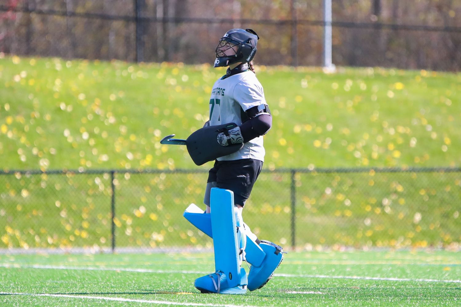 Field hockey players compete for possession of the ball during a match on a sunny autumn day.