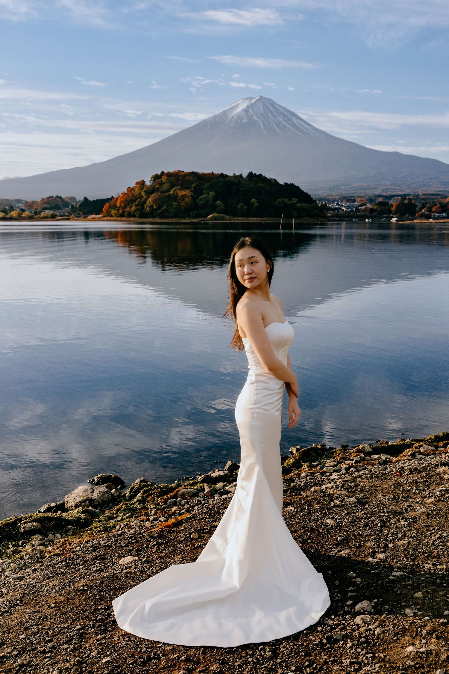A serene lakeside scene at Mount Fuji with a flowing white dress in the foreground and calm waters reflecting the sky.