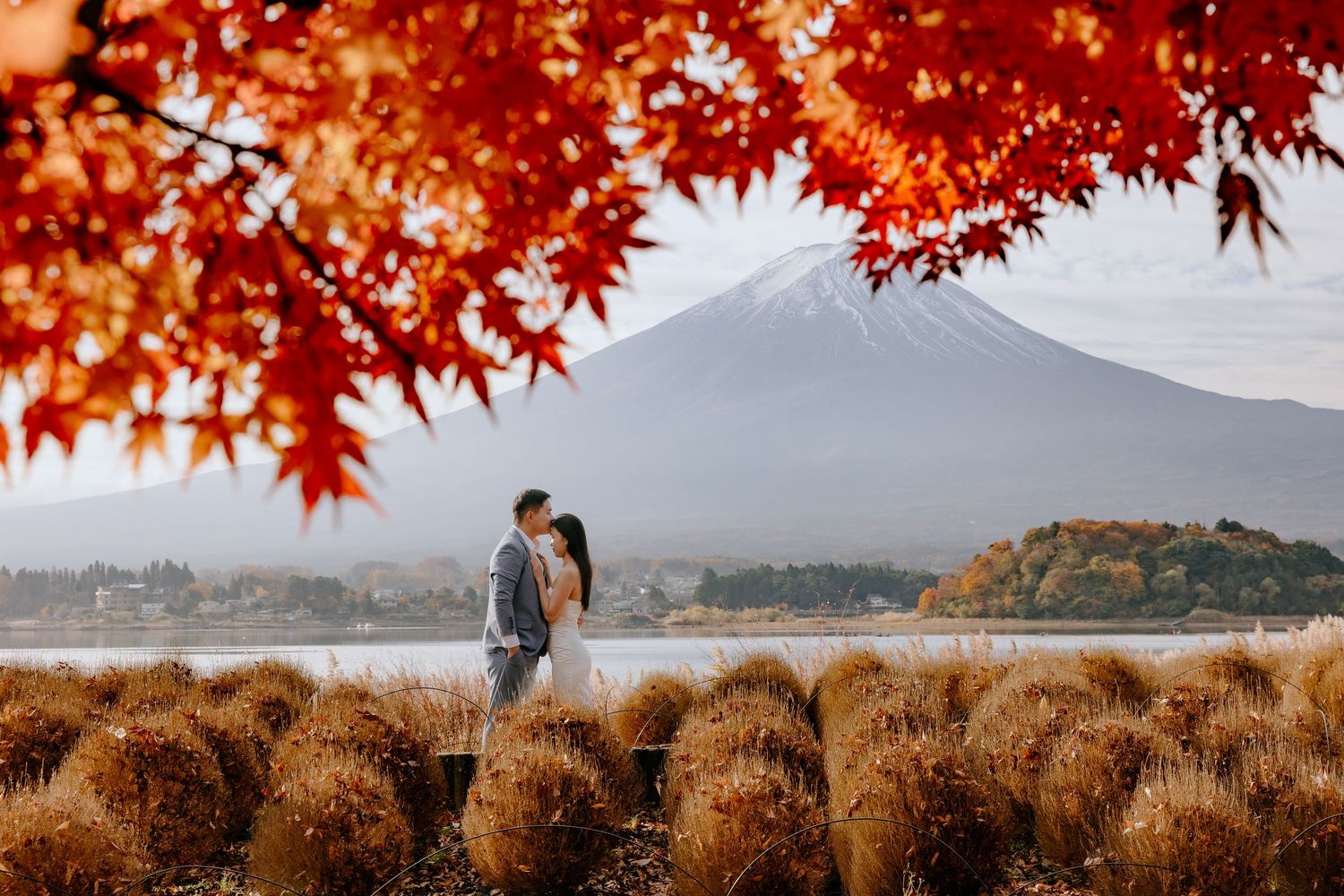 Vibrant red maple leaves frame scenic views of a mountainous autumn landscape with a lake in the background.