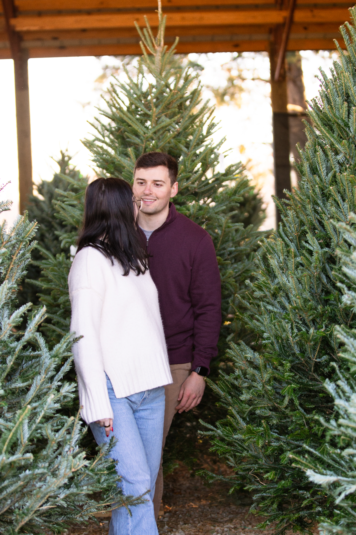 A couple shares a romantic moment while shopping for Christmas trees at a tree farm.