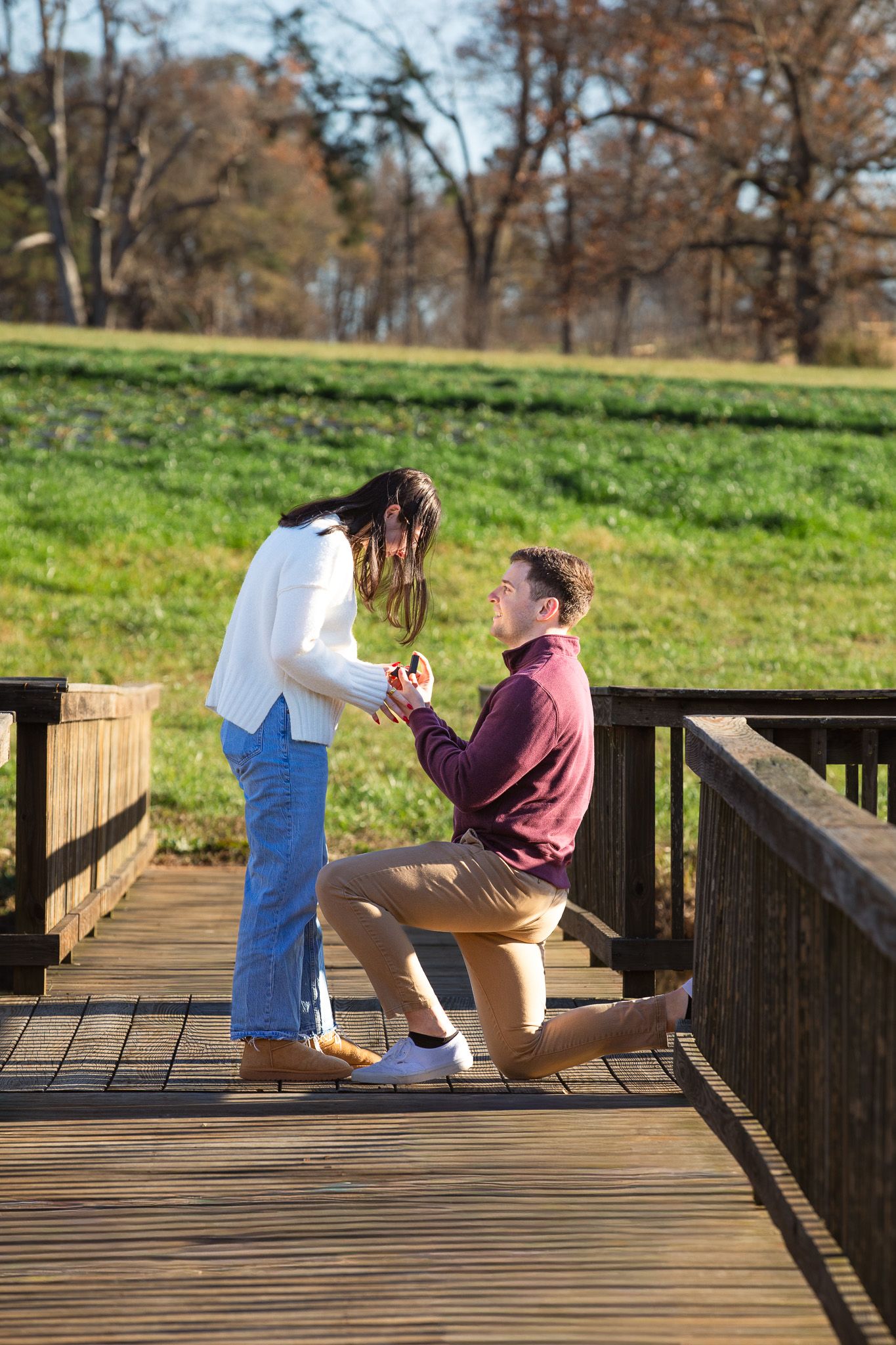 A couple sharing a romantic proposal moment on a wooden deck surrounded by autumn trees.