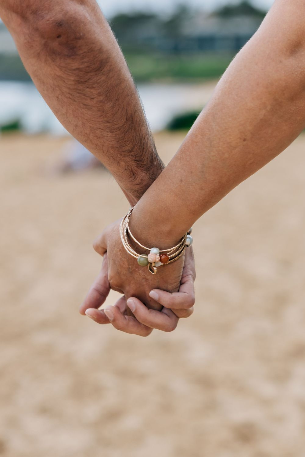 Couple holding hands on beach, woman wearing layered bracelets, close-up shot.