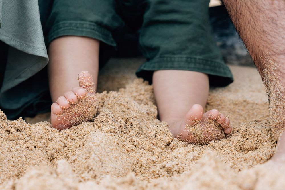Close-up of baby's sandy feet on beach next to parent's foot.