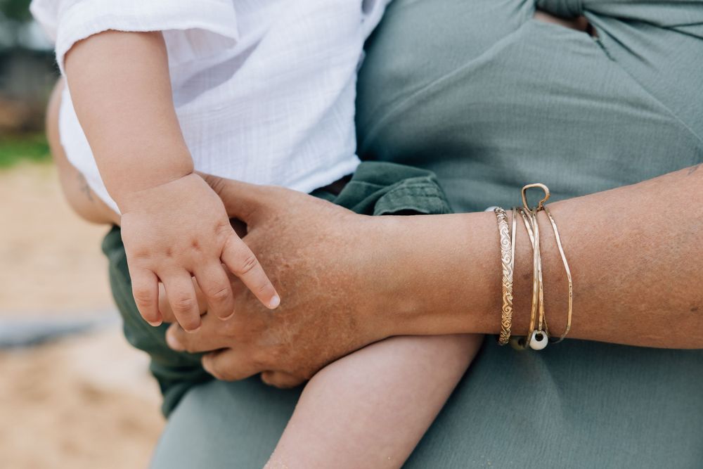 Close-up of mother holding baby's hand, wearing gold stacked bracelets.
