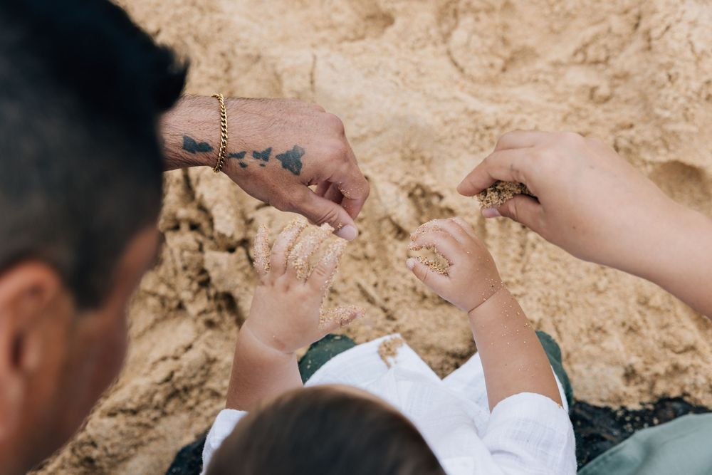 Family hands playing in sand at the beach together.