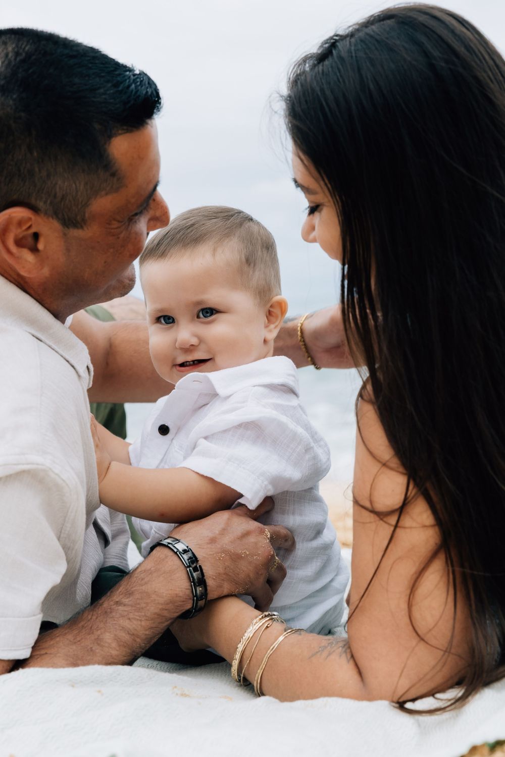 Parents lovingly gazing at their happy baby boy on the beach.