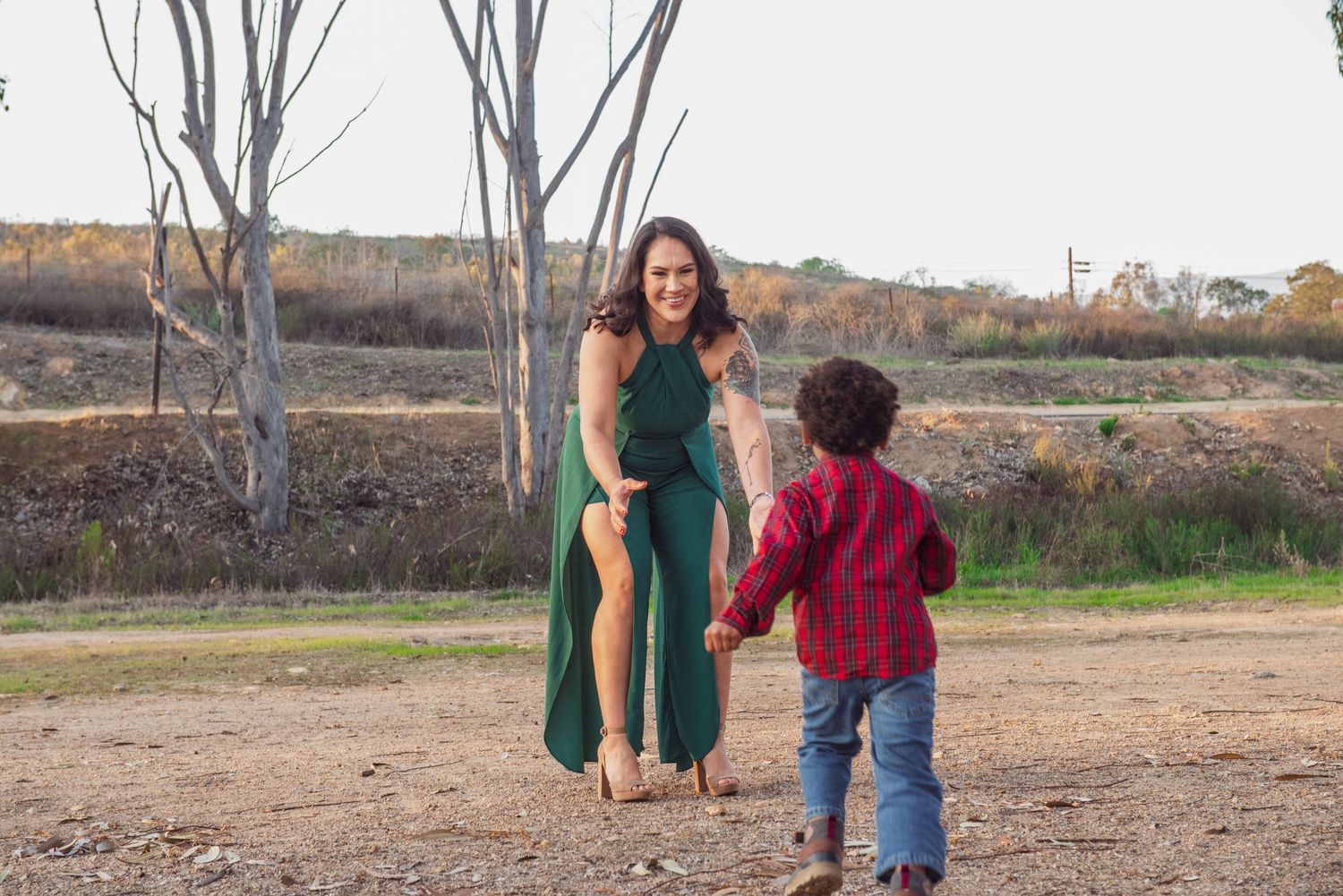 A parent and child in casual clothing walk together holding hands on a dirt path during autumn.