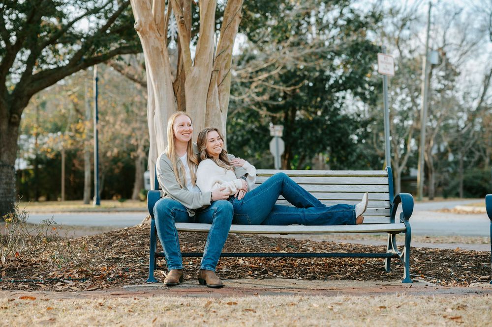 Couple sitting together on a wooden bench in a park during autumn with fallen leaves around them.