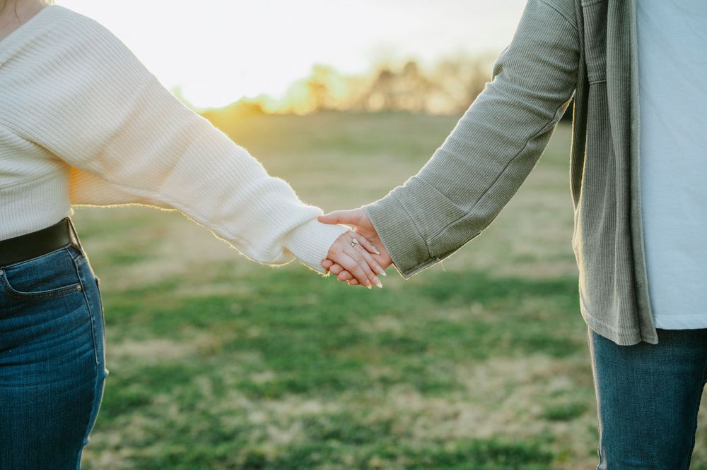 Couple holding hands while sitting on a wooden bench in a park with soft natural lighting.