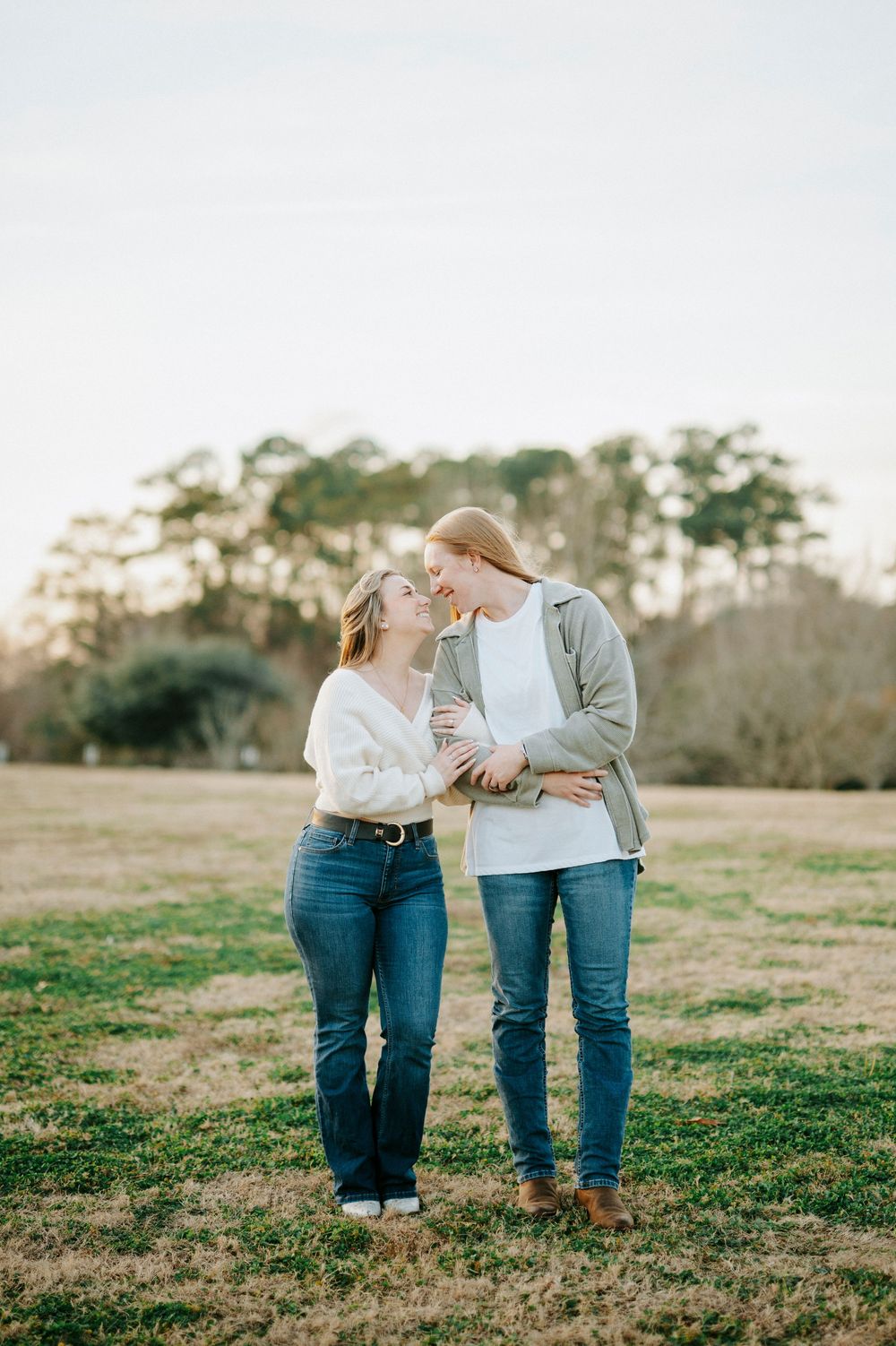 Couple in matching denim jeans and casual tops share intimate moments together in a grassy field at sunset.