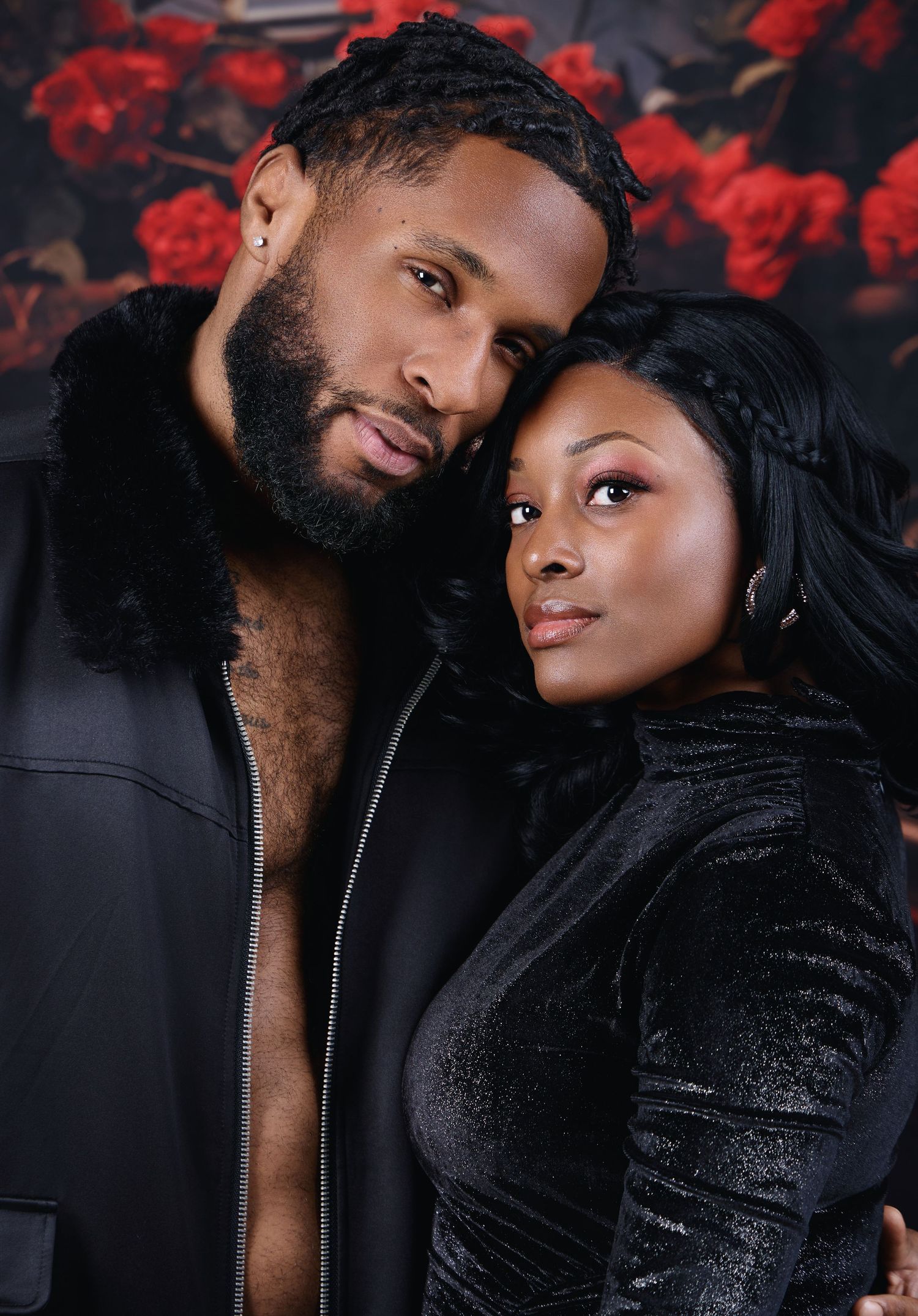 Intimate couple portrait in black outfits against dark floral backdrop.