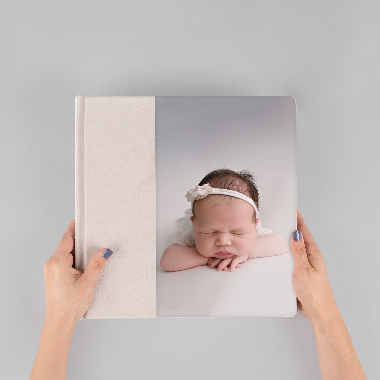 Hands opening a photography album showing baby portraits on light gray background.