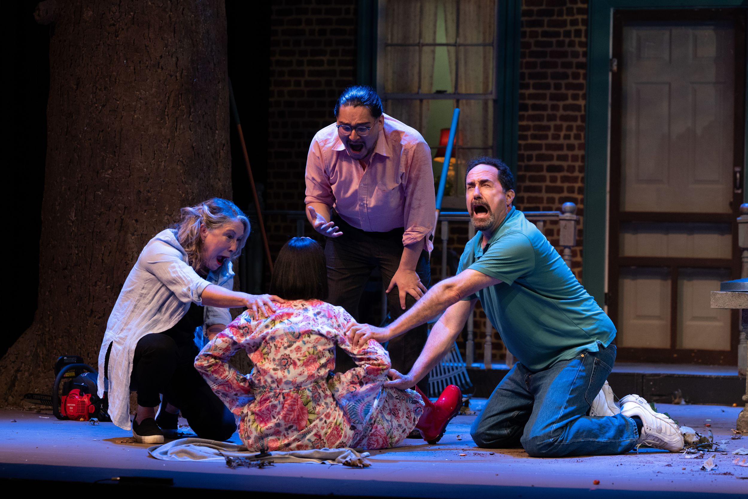 Theater actors performing dramatic scene on stage with brick building backdrop.