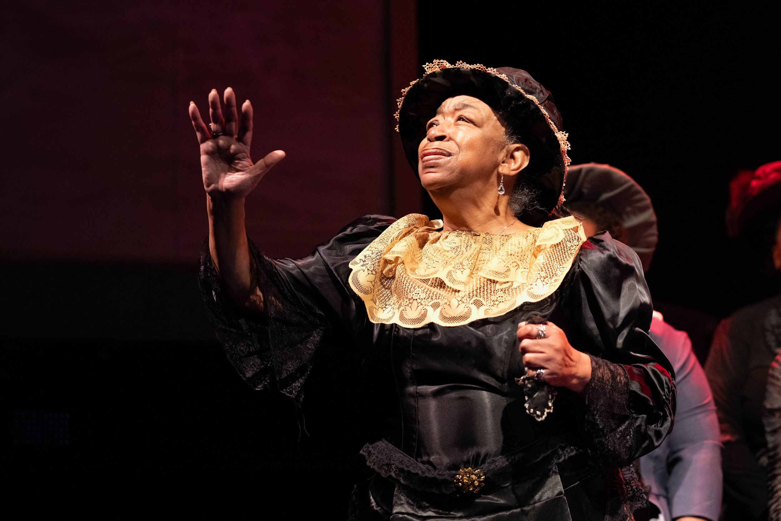 Dramatic theater scene showing performers in period costumes gesturing expressively on stage.